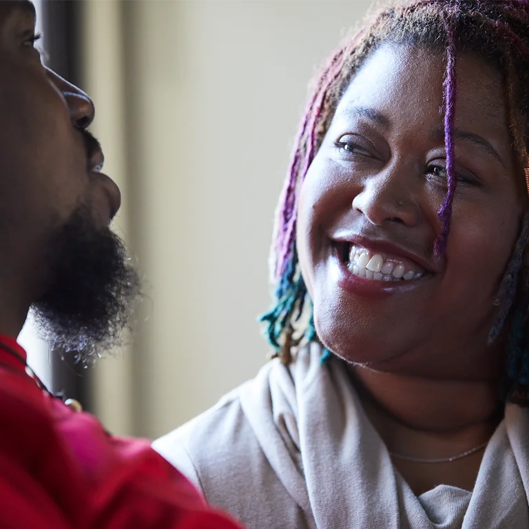 Black man and woman talking to each other. The Black woman has a large smile on her face.