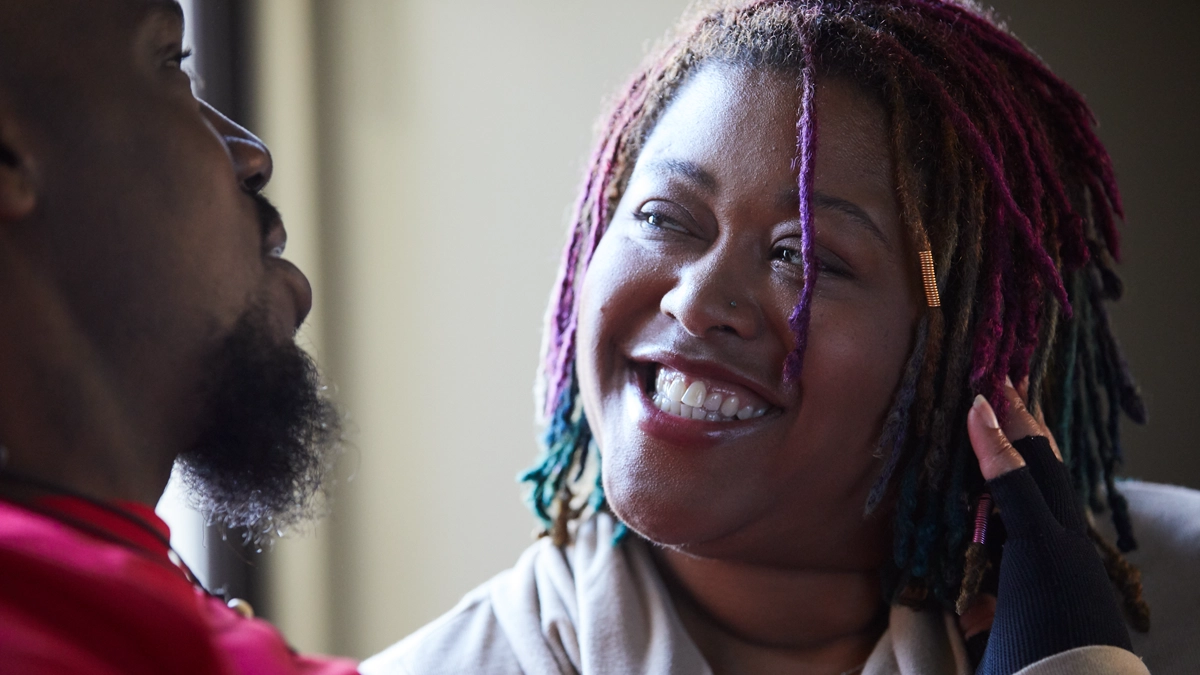 Black man and woman talking to each other. The Black woman has a large smile on her face.
