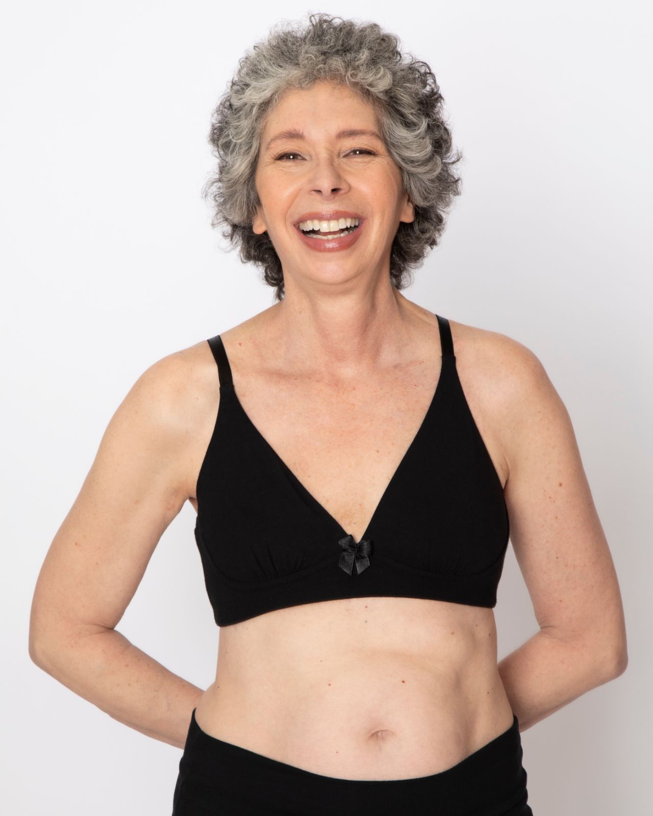 Older white woman smiling and wearing a black bra