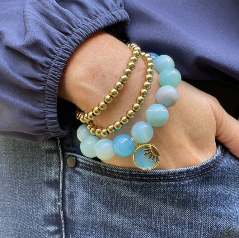 hand tucked into pocket, gold and blue beaded bracelets on the wrist