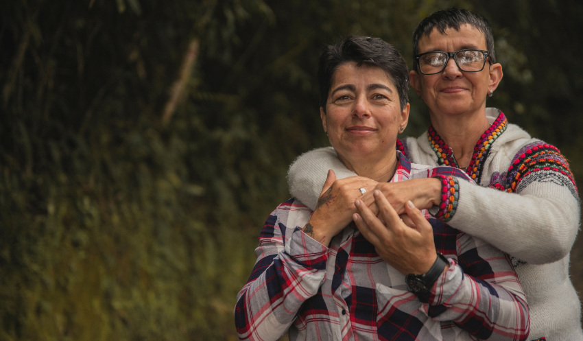 An older lesbian couple dressed in flannel embraces