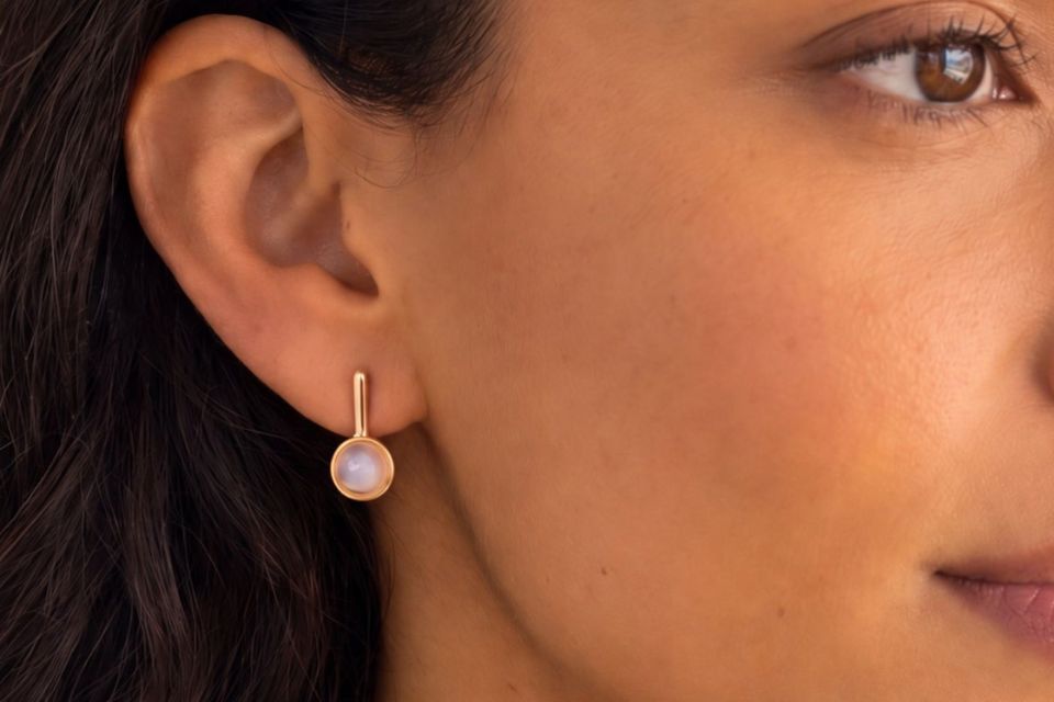A Latina woman wearing gold dangly earrings with a pin stone