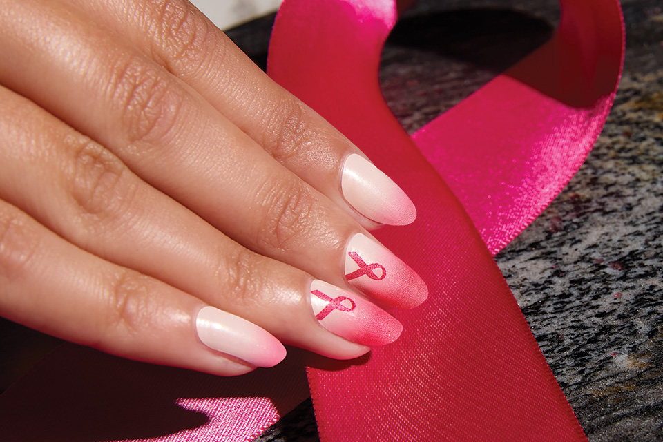 A close up of a Black woman's nails that are a white/pink gradient with a pink ribbon on the two middle nails.