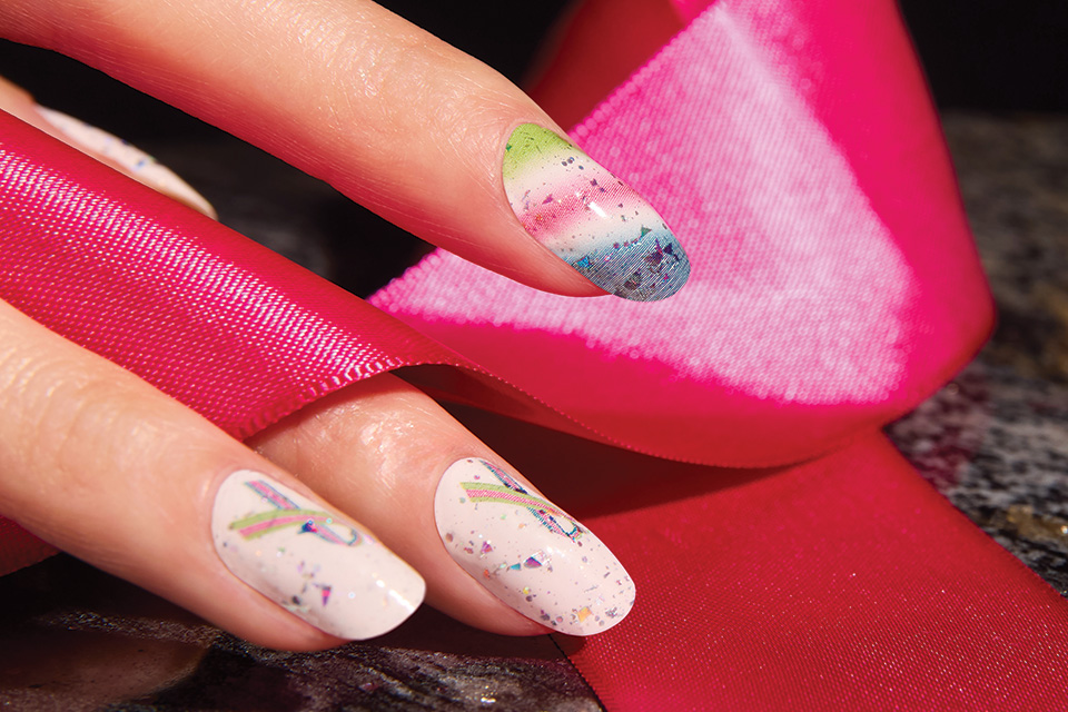 A close-up of a white woman's nails that are rainbow colors and have rainbow colored ribbons on them.