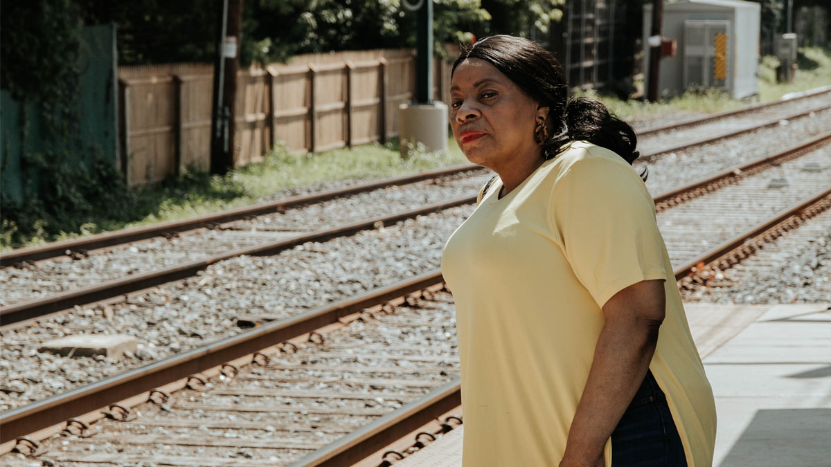 A woman standing at an empty trolley station, looking down the tracks.