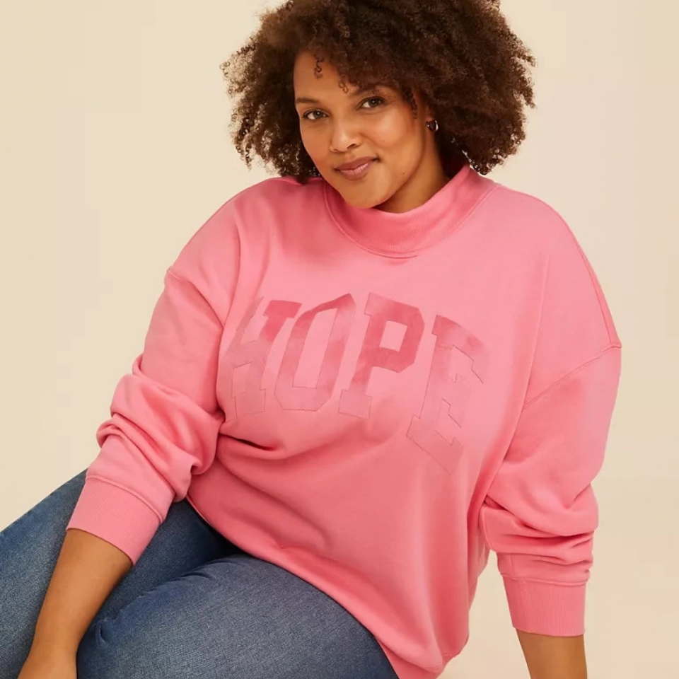 A Black woman wearing a pink mock neck that says 