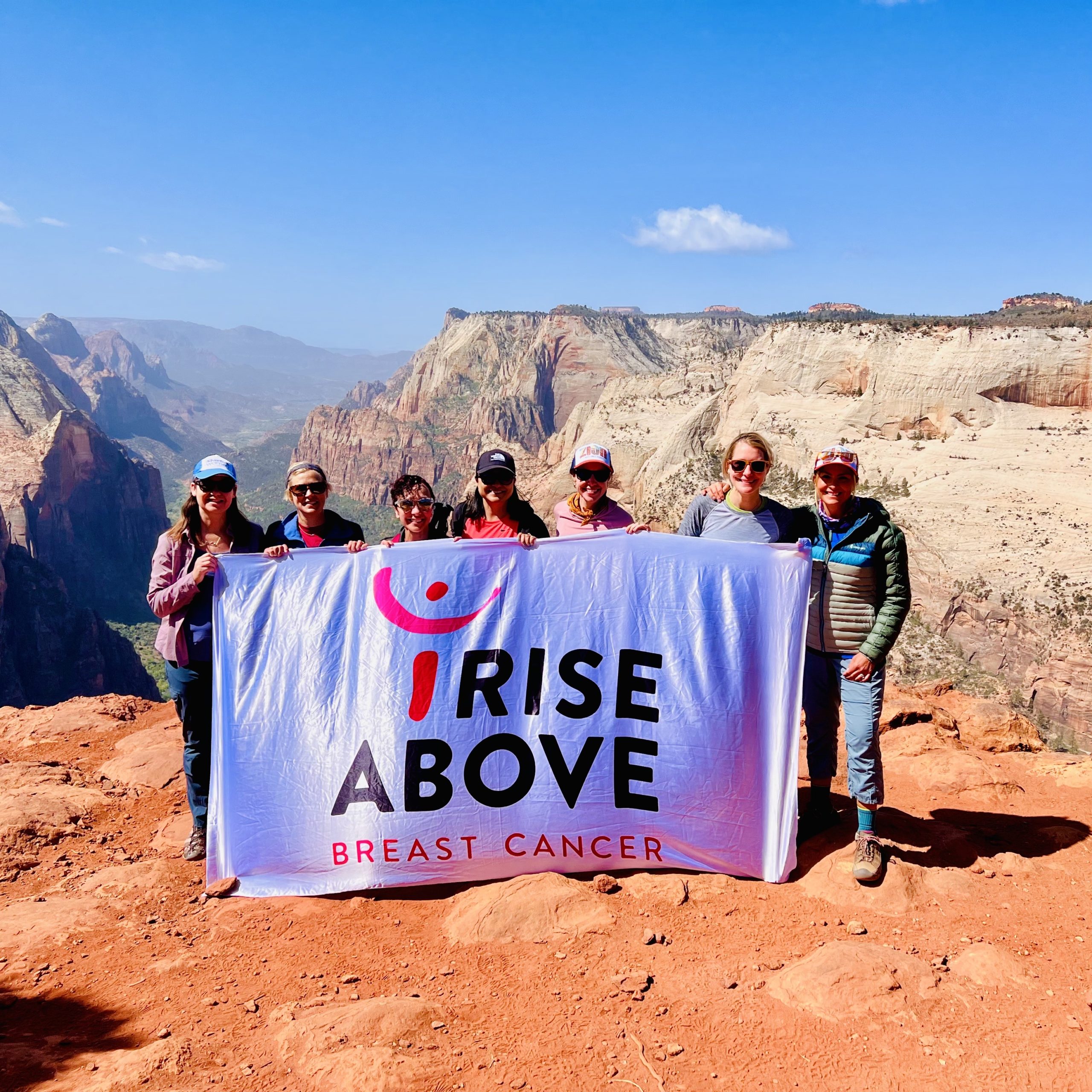 Seven women posing with a large iRise Above Breast Cancer sign in the mountains of Utah