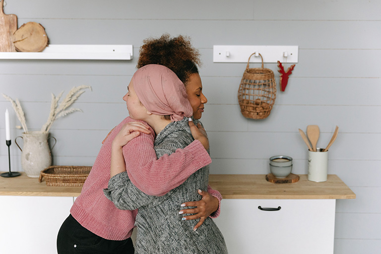 Two women hugging. One woman has a wrap on her head.