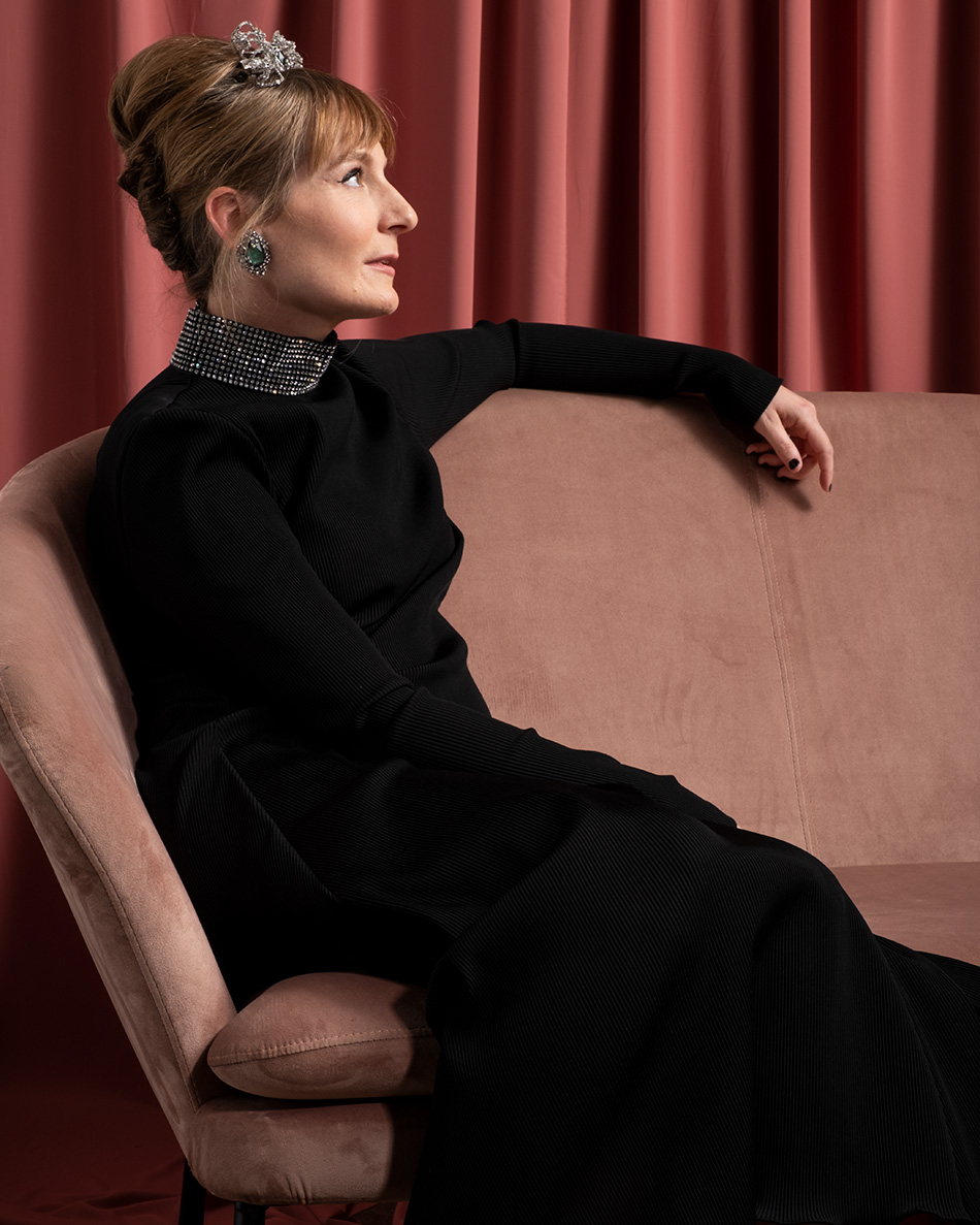 Kerri sits on a couch in a formal black gown and a tiara on her head. Photo by Ken Cox and Andrew Scherer from Kronus Studio
