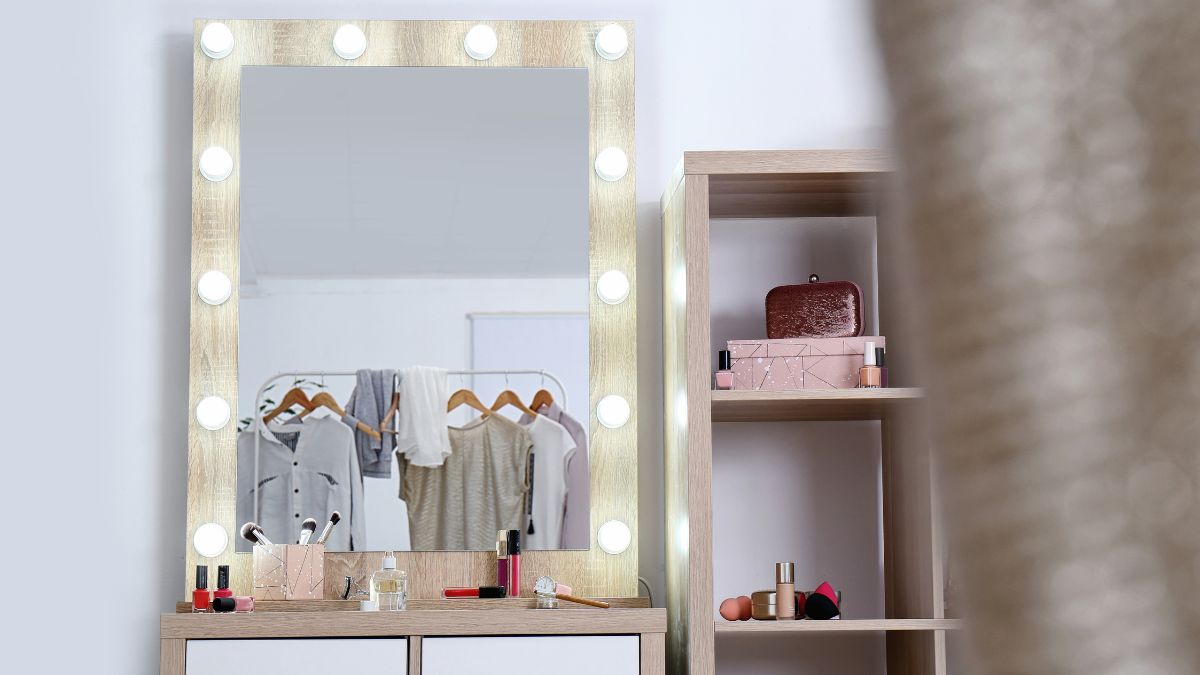 Lights illuminate a dressing room mirror, a rack of women 's clothing in the reflection.