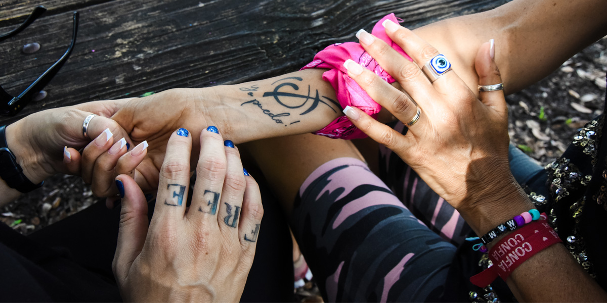 Closeup of four hands. One hand has "FREE" tattooed on the fingers. One arm has "Yo puedo!" tattooed on it. Photo by AK Cespedes.