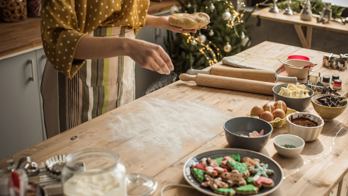 Woman spreading flour on a baking surface with cookie ingredients and baked holiday cookies