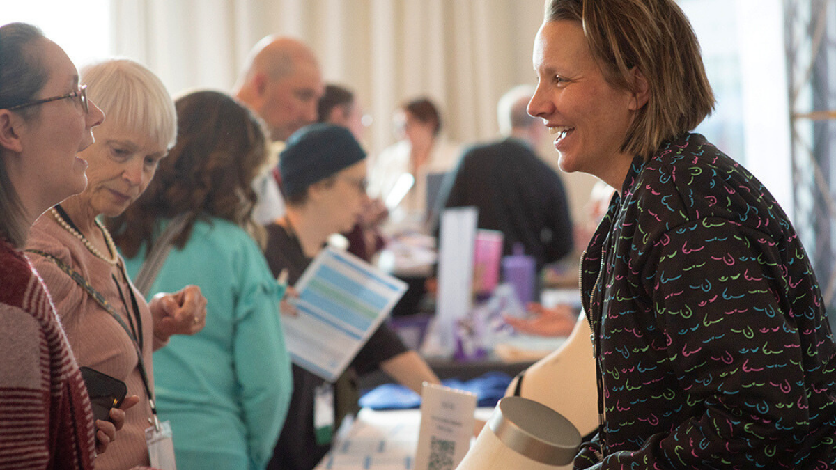 Dana Donofree of AnaOno smiling and talking to conference participants at the exhibitor showcase.