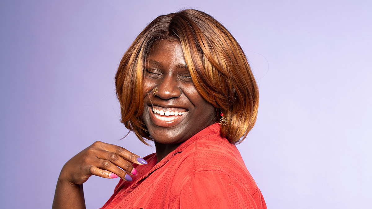 A Black woman smiling with her hand touching her chest.