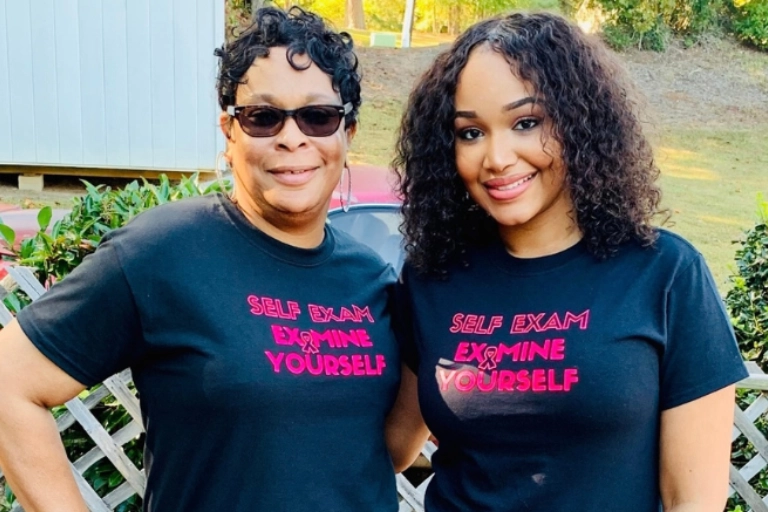 Two Black women, a mother and daughter, both wearing shirts saying "Self Exam / Examine Yourself"