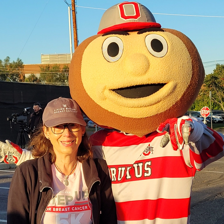 Linda in a baseball cap with Brutus Buckeye, the Ohio State mascot, who wears a red and white striped shirt and baseball cap with the letter 'O".