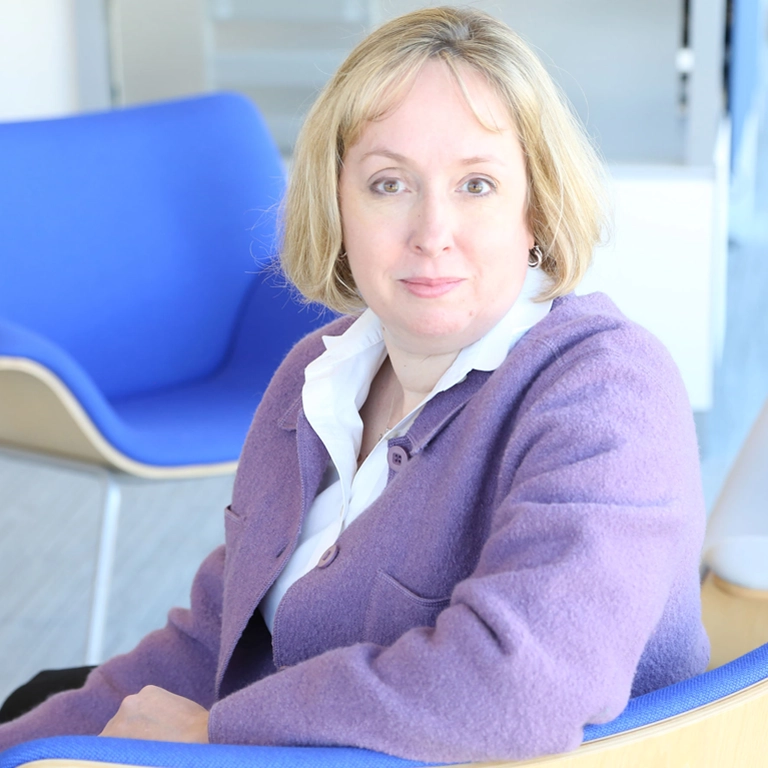 Blonde bobbed Pam Traxel in white collared shirt and lilac blazer.