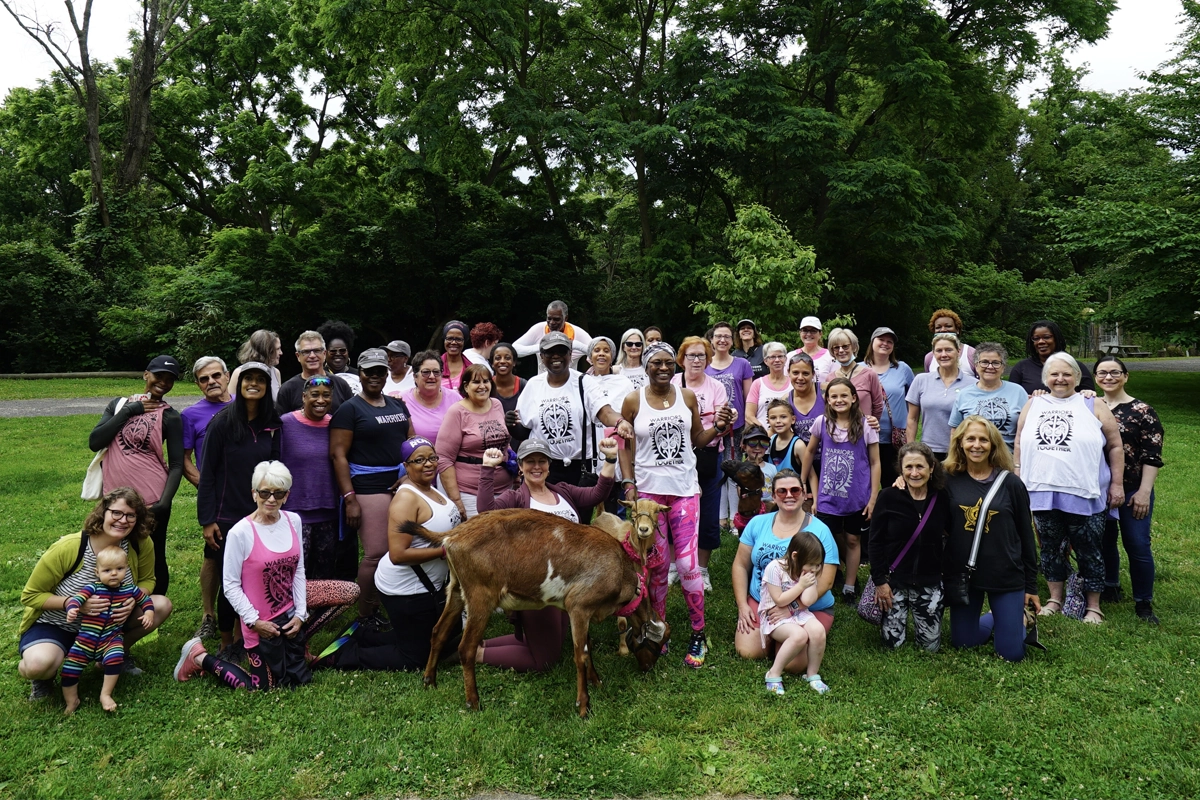A large, diverse group of people gather in a green field on a bright day