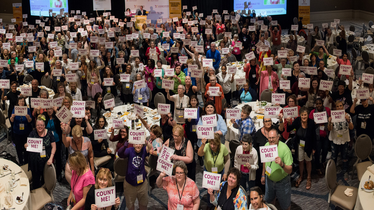Attendees of the 2017 Conference on Metastatic Breast Cancer hold up signs saying, "Count me"