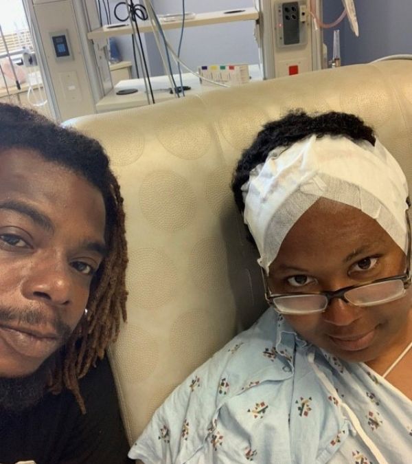With her husband at her side, Cheryl sits in hospital bed with bandaged scalp