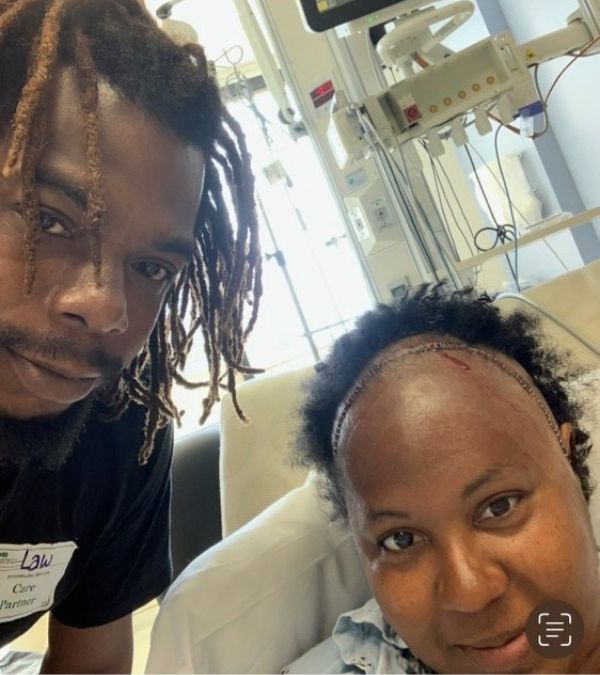 Her husband beside her, Cheryl sits up in hospital bed and shows the stitches on her scalp