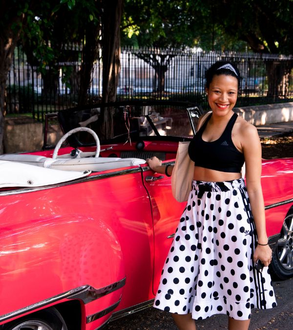 A young Black woman stands by a vintage car in Cuba