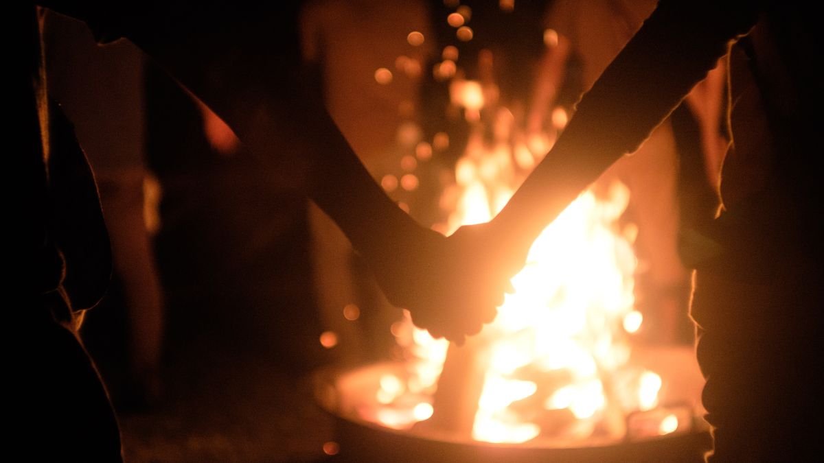 Two clasped hands in front of an glowing campfire at night.