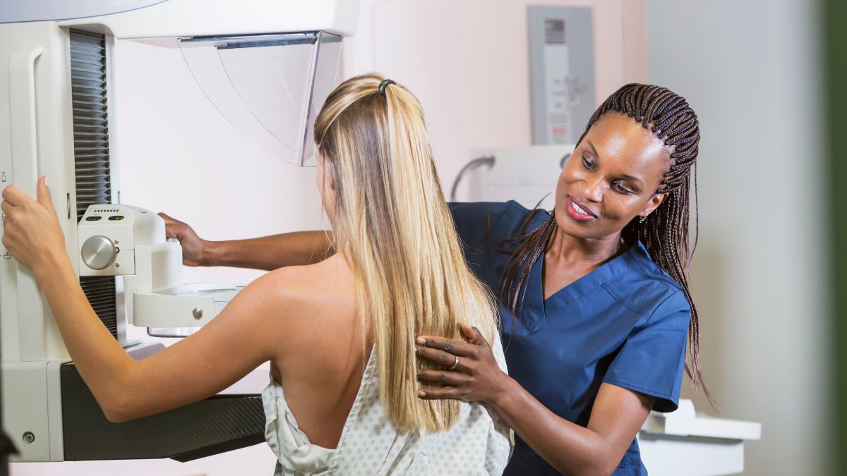 Young black woman gently administers a mammogram to a young white woman with blond hair