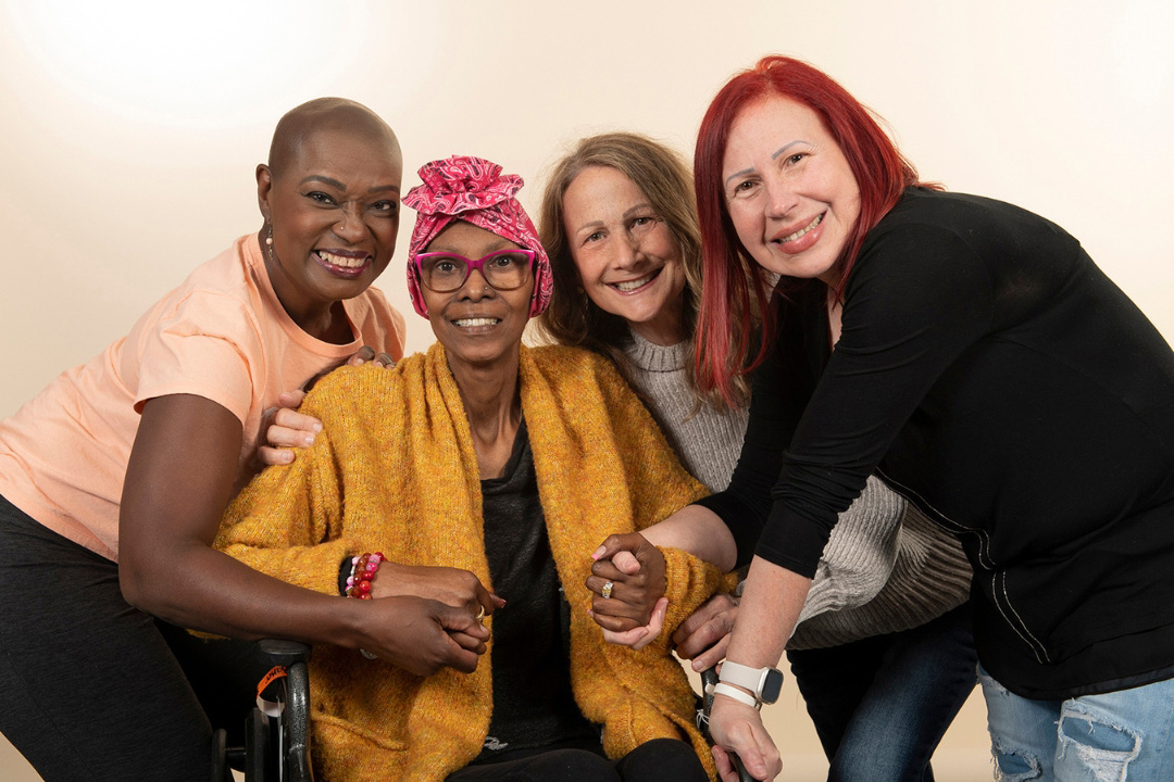Group of four women, 2 Black and 2 white, holding hands. One woman is in a wheelchair.