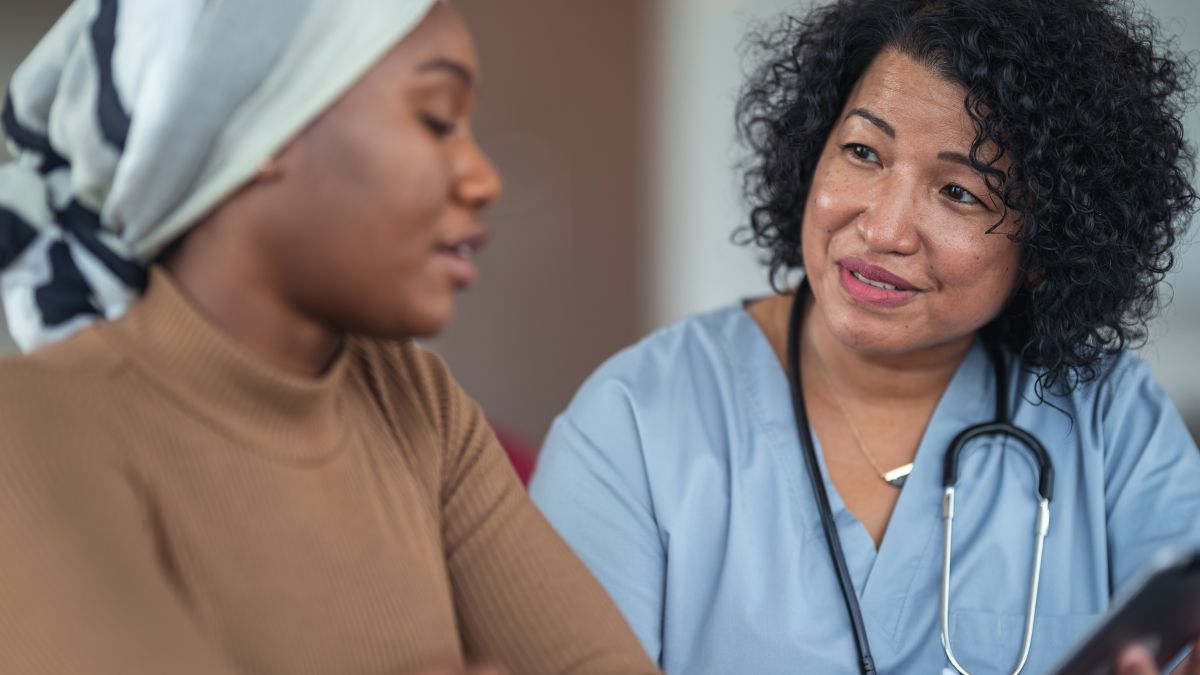 Black female nurse speaks with young Black woman with headscarf