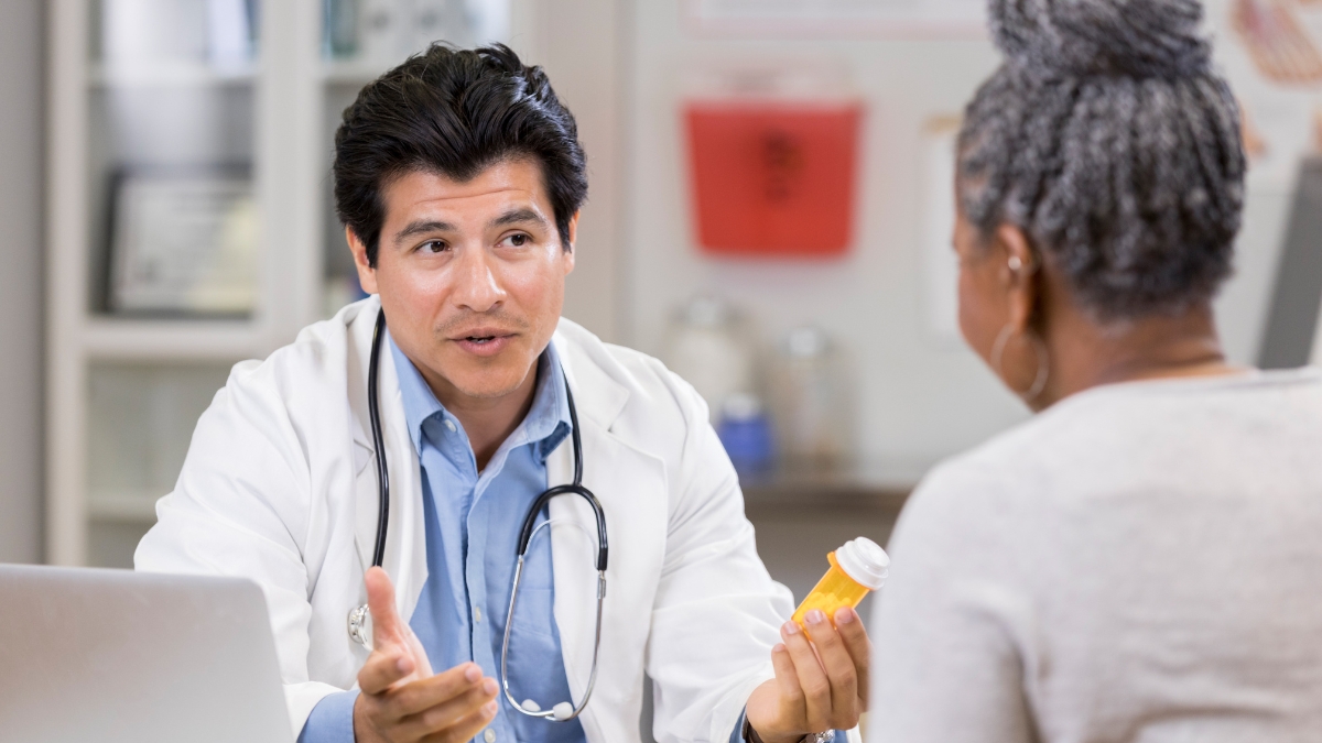 Asian male doctor talking to black female patient while holding a bottle of medicine