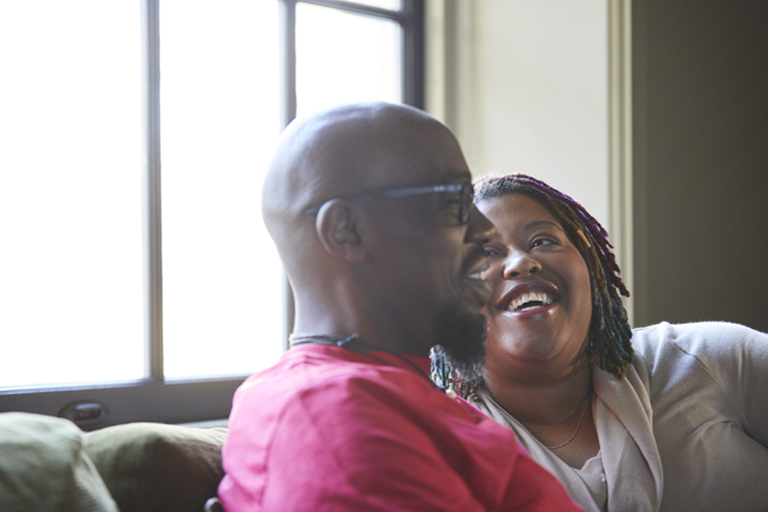 A Black man and woman sit on a couch, laughing together