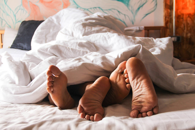 Feet of two people tangled up in bed, under covers