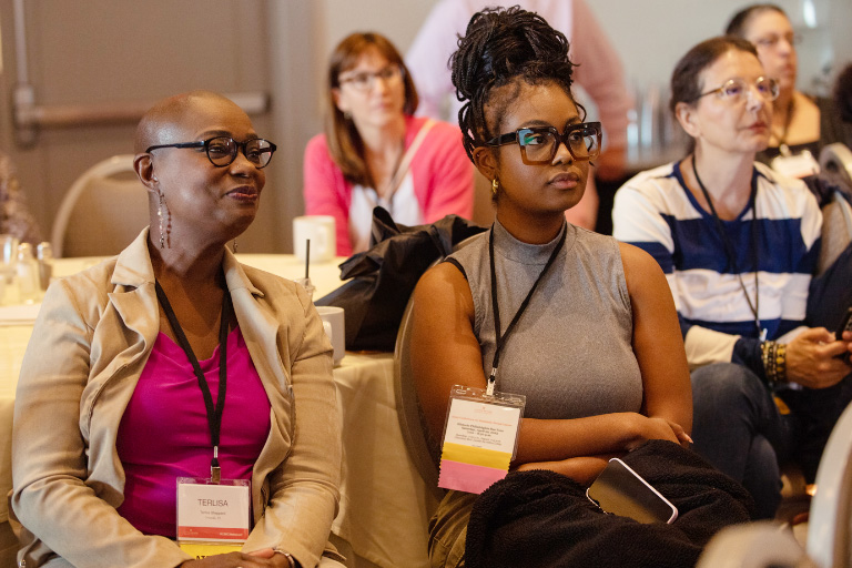 Two Black women listen to a talk at the 2023 Conference on Metastatic Breast Cancer