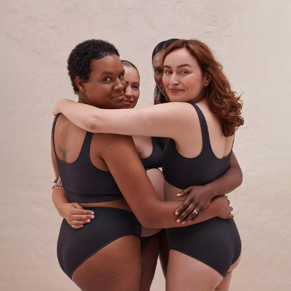four women wearing black underwear, hugging