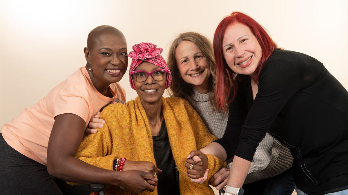 A diverse group of four women holding hands and smiling.