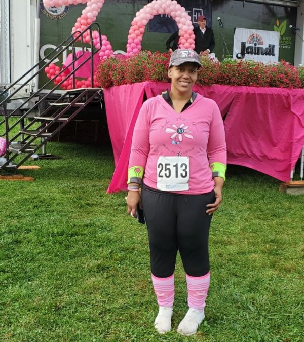A Black woman poses in front at a Pink Breast Cancer event stage