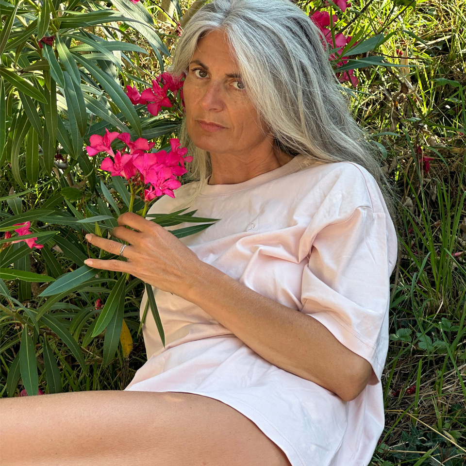 A woman posing in a light pink t-shirt next to flowers.