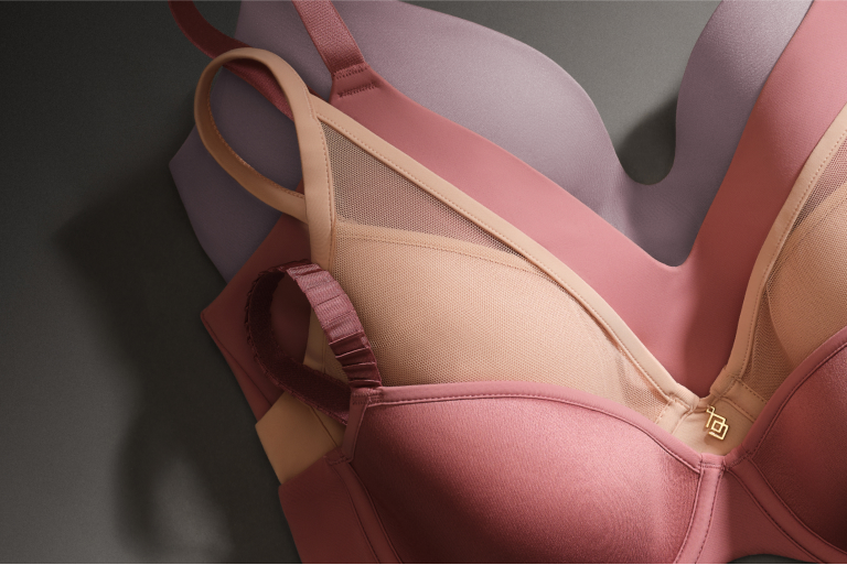 Four bras laying on top of each other. Two are pink, one is tan, and one is purple.
