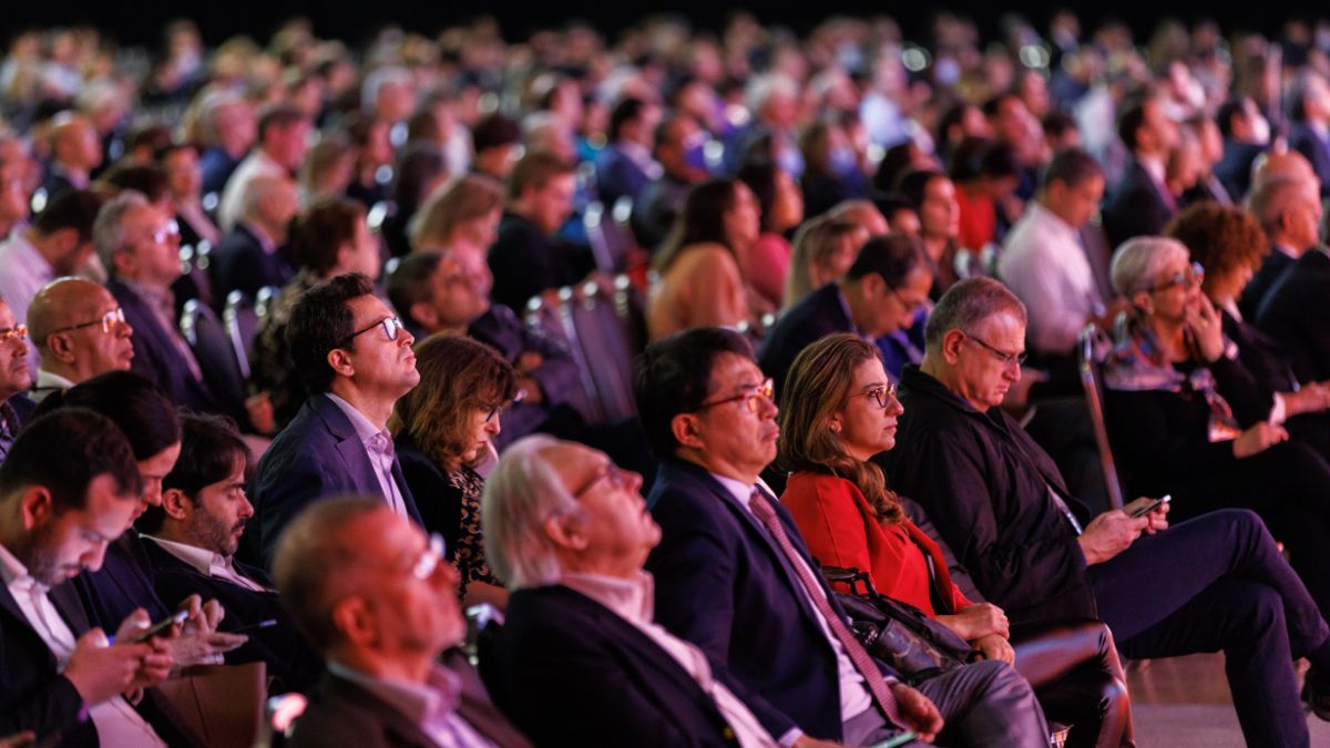 A full house of attendees sit in rapt attention at a conference.