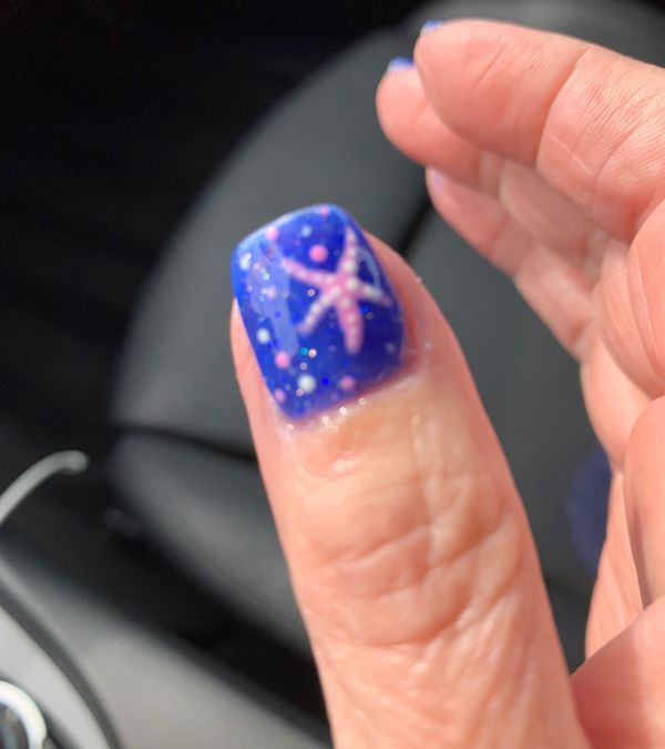 A manicured thumb with purple nail polish and a starfish design