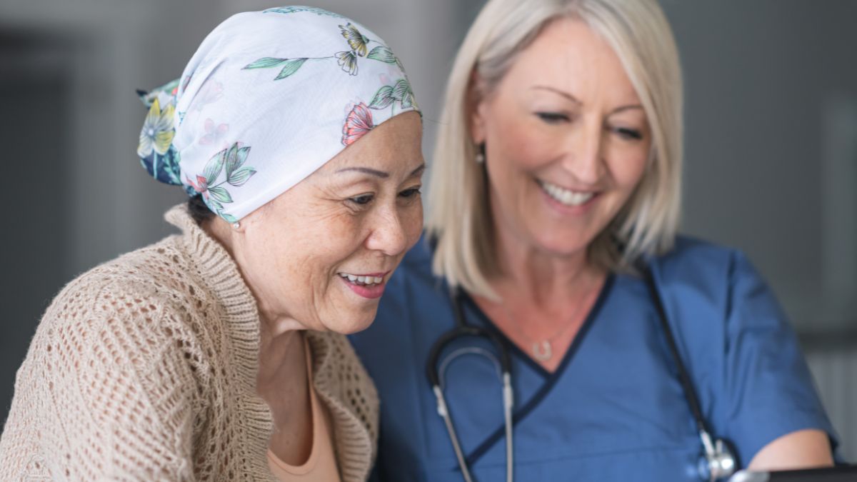 An older Asian woman with a headscarf and a healthcare provider smile as they look at something together