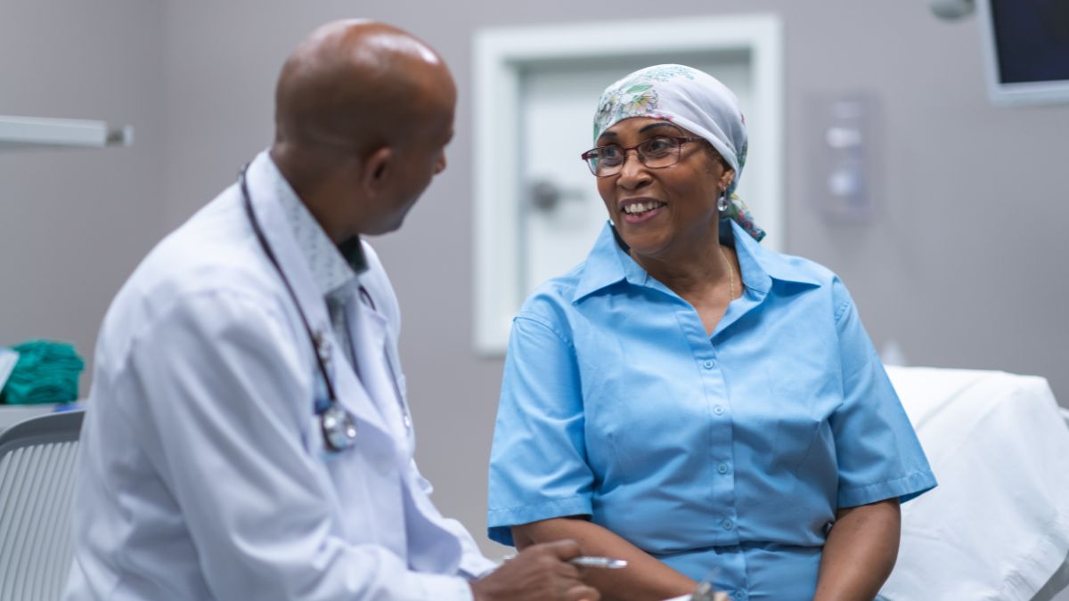 An older Black woman talks with a Black male doctor.