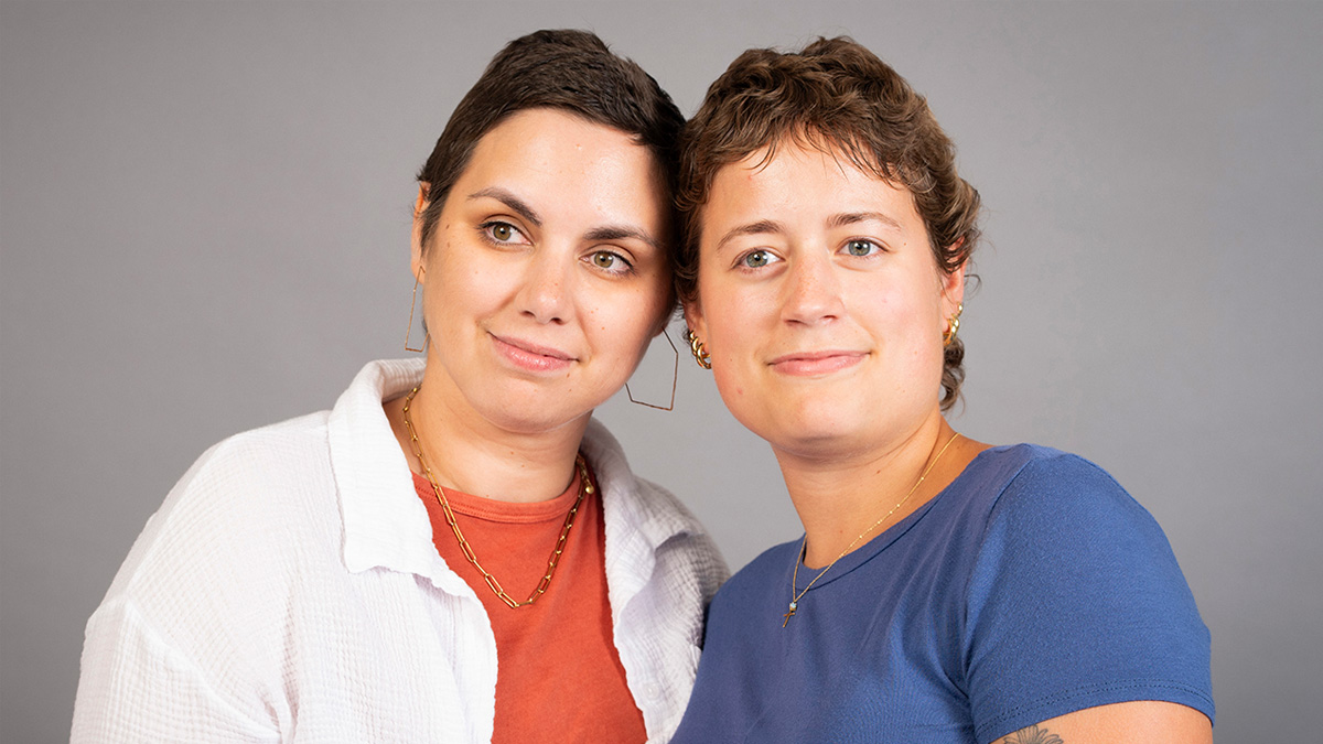 Two young white woman with pixie haircuts, smiling with their heads touching.