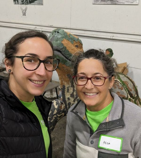 A dinosaur statue peeks in between Alicia Legendijk and a young white woman