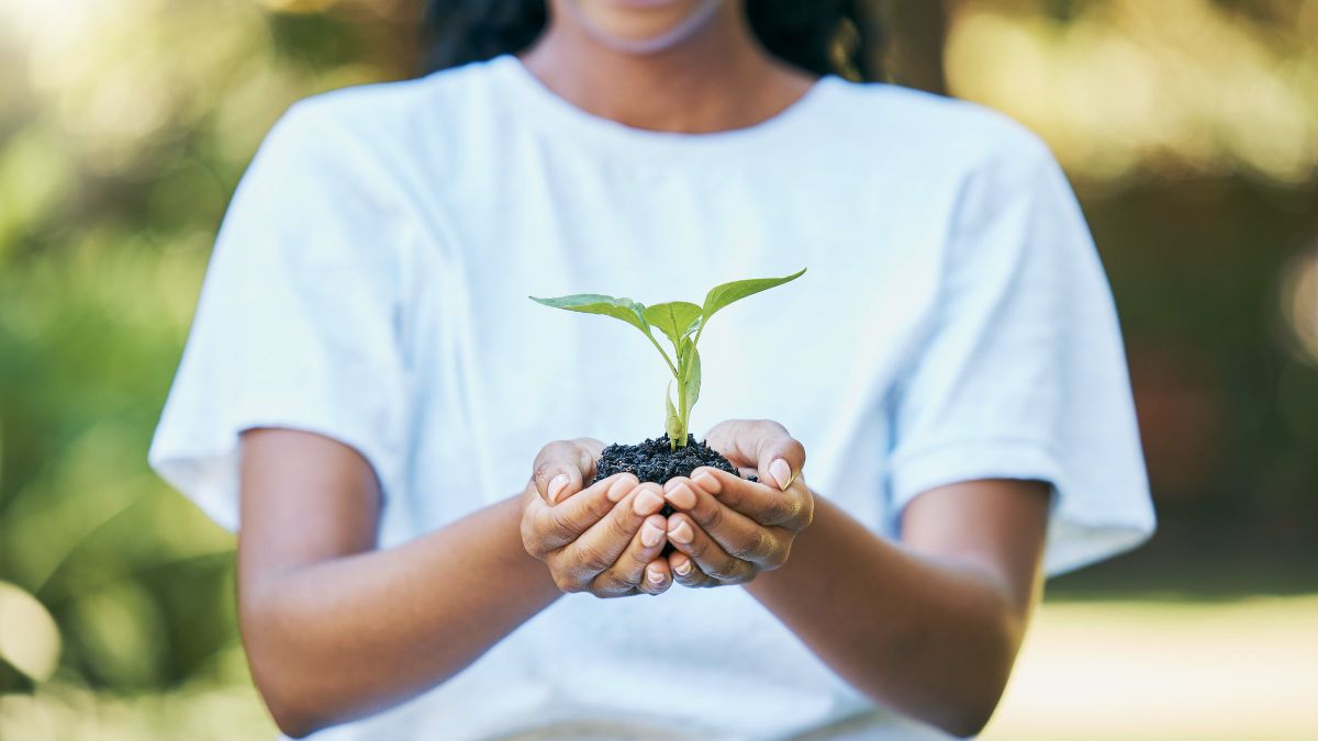 A tiny plant is held gingerly by a smiling Black woman