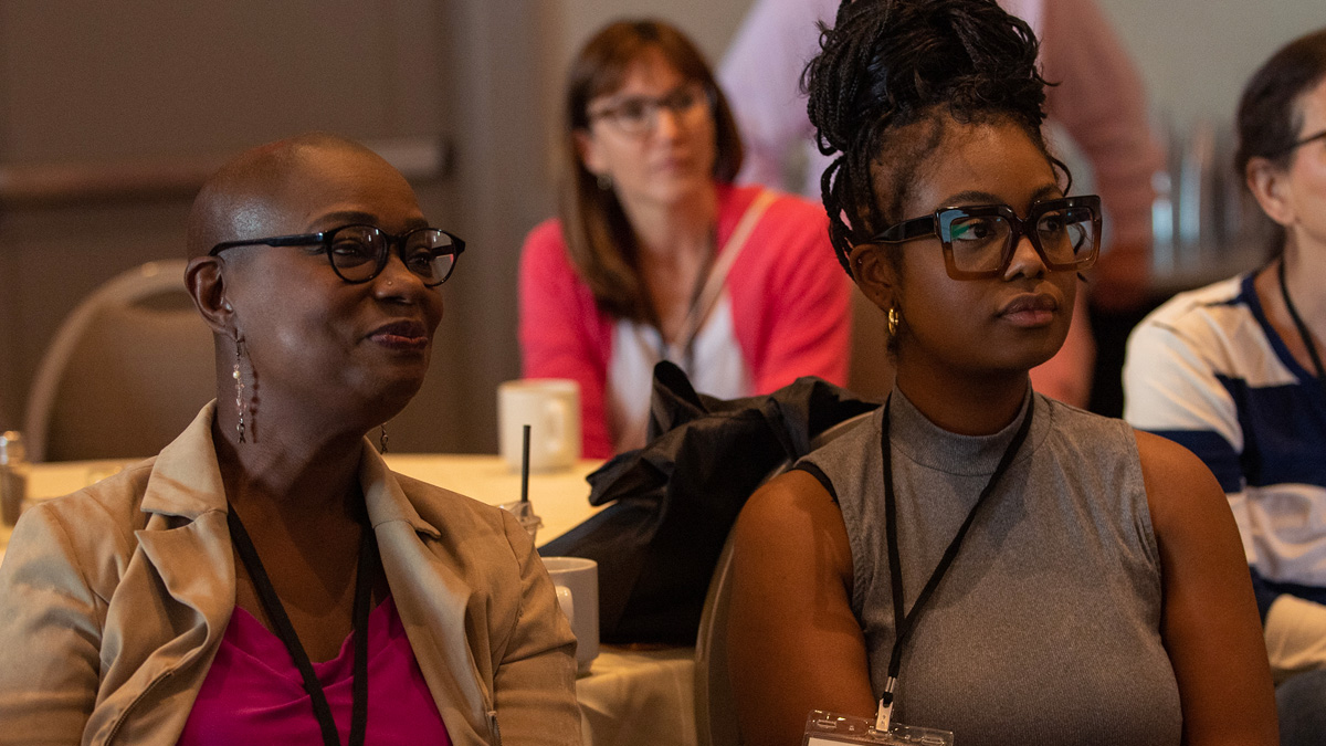 Two Black women listen to a talk at the 2023 Conference on Metastatic Breast Cancer