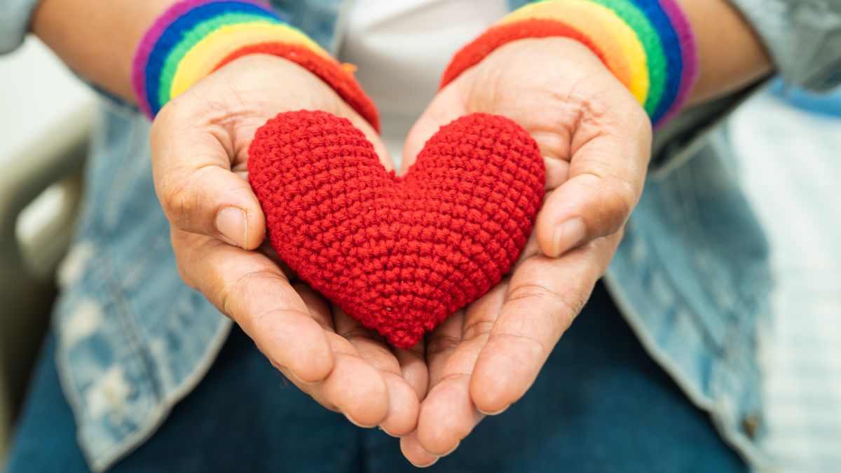 Two hands with rainbow wristbands hold a crocheted red heart