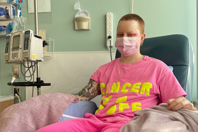 A masked Mike Hooves sits in a chemo chair, bright and defiant in pink