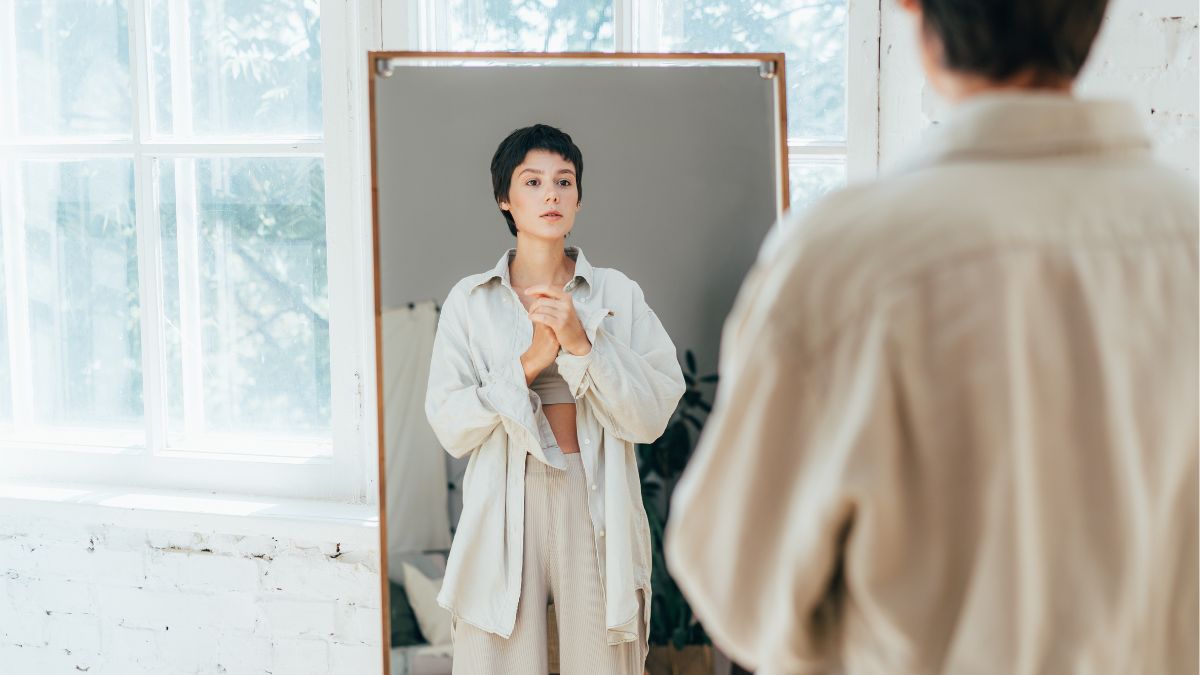 A woman with short hair looks at herself in a mirror